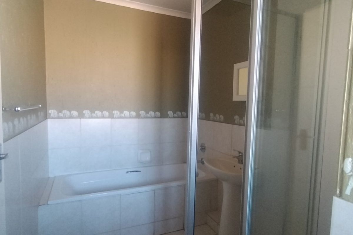 A functional bathroom featuring a built-in bathtub, a separate shower enclosure, and a pedestal washbasin with tiled finishes.