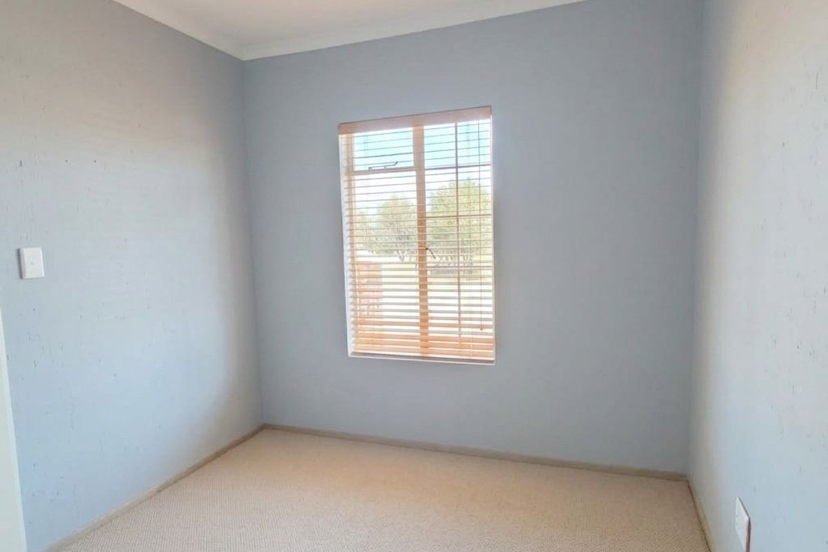 A clean, empty bedroom featuring neutral carpeting and fitted window blinds, providing a blank canvas for personalization.