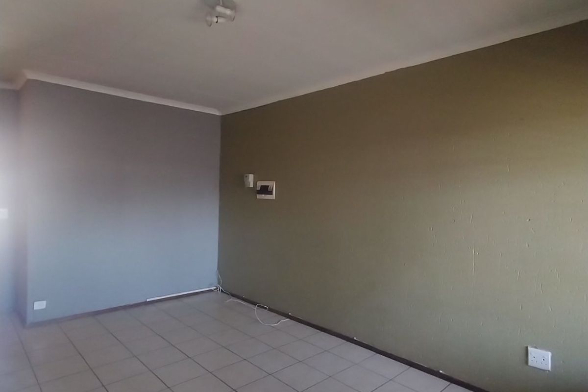 An empty living room featuring neutral tiled flooring and dual-tone painted walls, equipped with an intercom system and ceiling lighting.