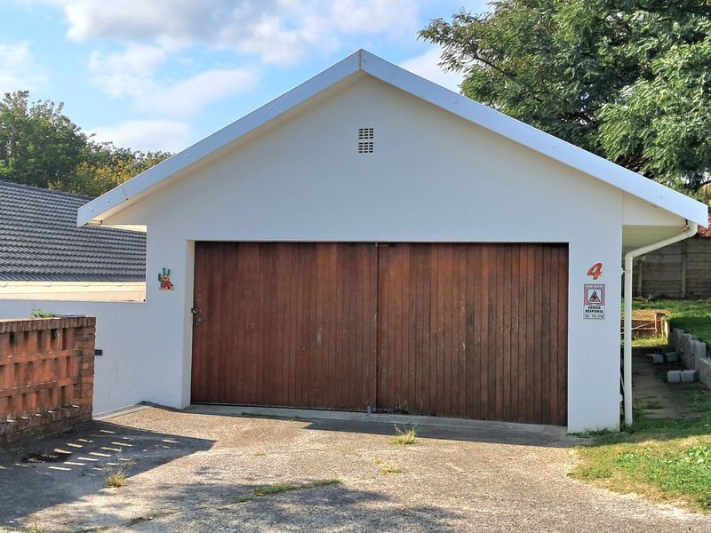 A detached garage featuring a wooden door, concrete driveway, and brick boundary wall, set within a residential property.