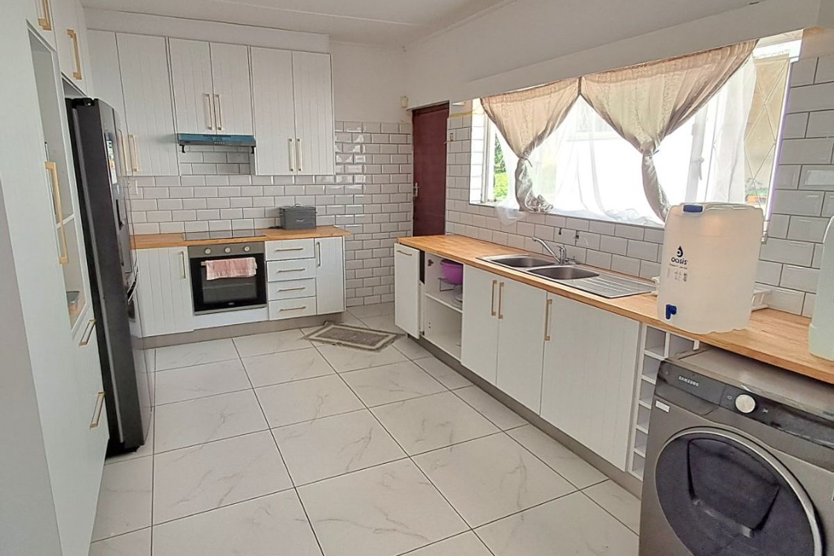 A bright, modern kitchen featuring white cabinetry, subway tile backsplash, wooden countertops, and tiled flooring with integrated oven and extractor fan.