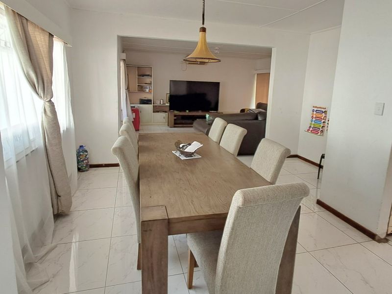 Open plan dining and living area featuring light-colored tiled flooring and a central pendant light fixture, creating a connected and functional living space.
