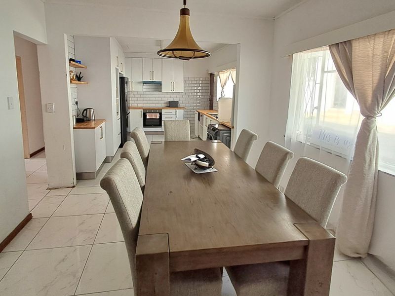 Open plan dining and kitchen area featuring modern tiled flooring, white cabinetry, subway tile backsplash, and integrated kitchen appliances.
