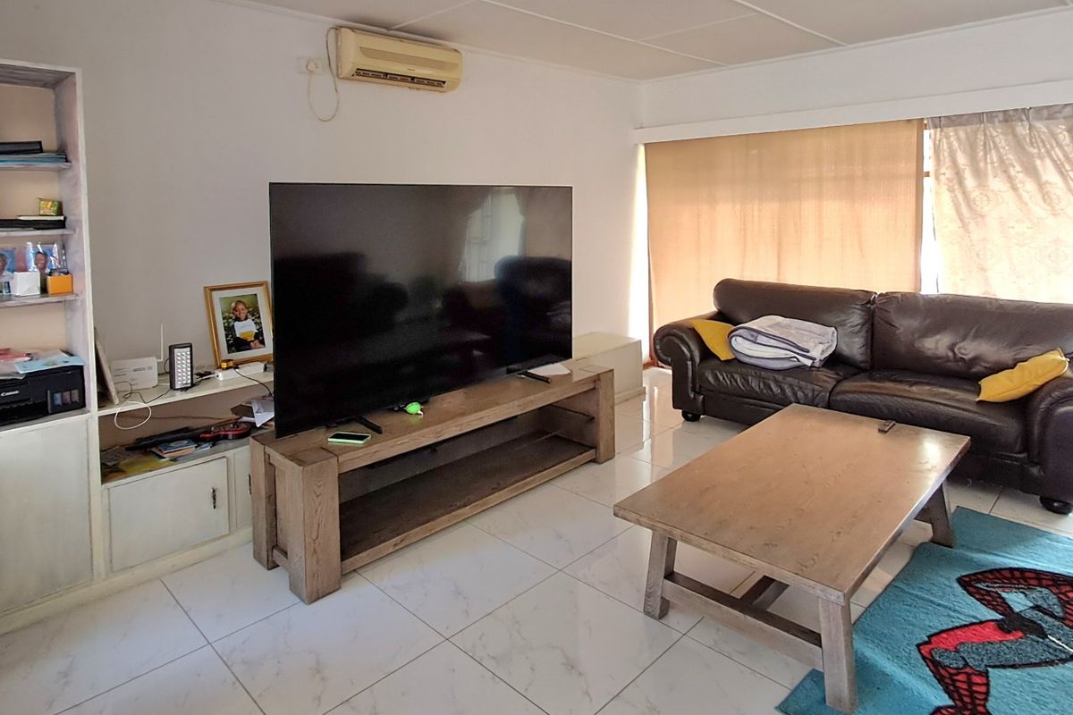 A living room featuring white tiled flooring, a built-in shelving unit, and a wall-mounted split-system air conditioner.
