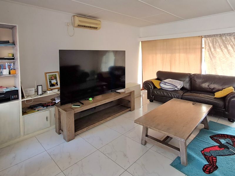 A living room featuring white tiled flooring, a built-in shelving unit, and a wall-mounted split-system air conditioner.