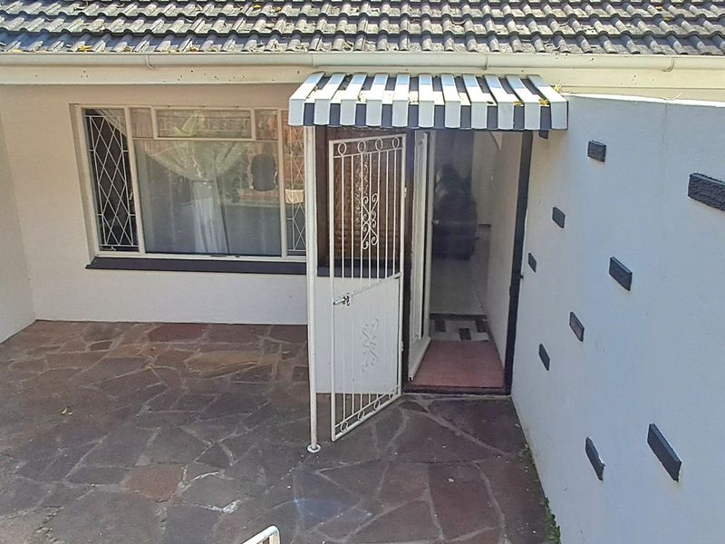 Front entrance area featuring a stone paved patio, security gate, and a striped awning over the doorway.