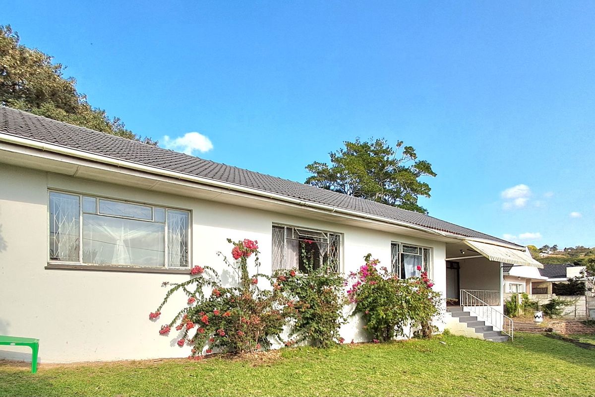 Rear exterior view of a single-story house featuring a tiled roof, security-barred windows, and a small concrete patio area with an awning.