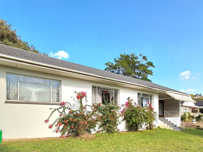 Rear exterior view of a single-story house featuring a tiled roof, security-barred windows, and a small concrete patio area with an awning.