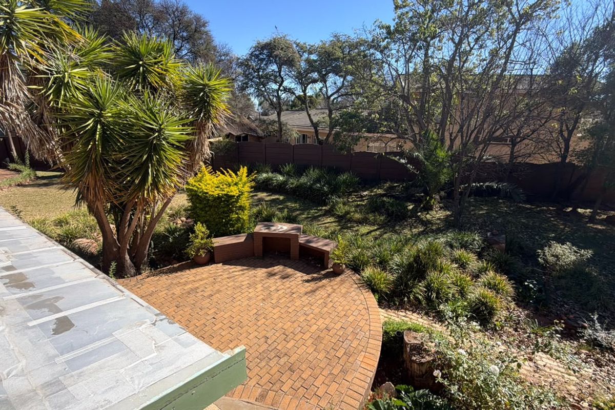 A private rear garden featuring a circular brick-paved patio with built-in seating, surrounded by established trees and perimeter fencing.