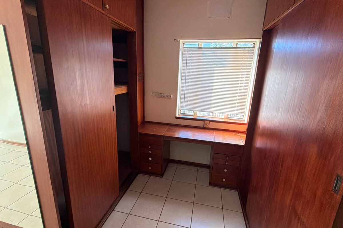 A bedroom featuring extensive built-in wooden cabinetry and a integrated desk area with tiled flooring and natural light.