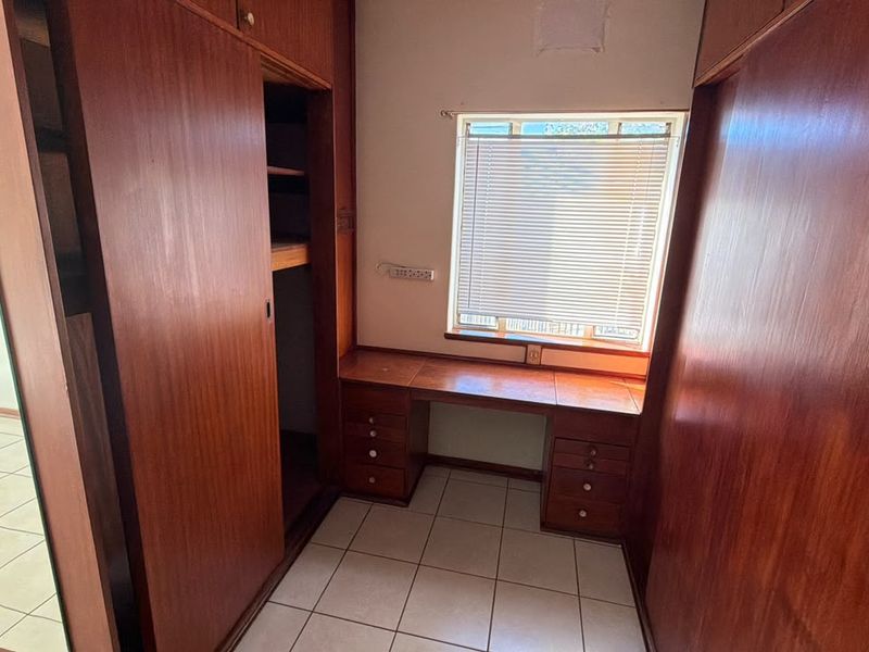 A bedroom featuring extensive built-in wooden cabinetry and a integrated desk area with tiled flooring and natural light.