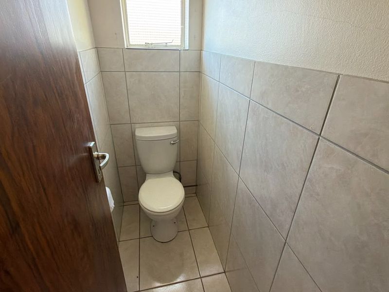 A compact, functional guest toilet featuring neutral wall and floor tiling and a window for natural ventilation.