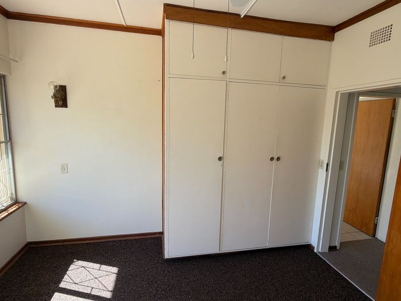 A vacant bedroom featuring built-in cupboards, timber trim details, and large windows, offering a blank canvas for renovation and interior design updates.