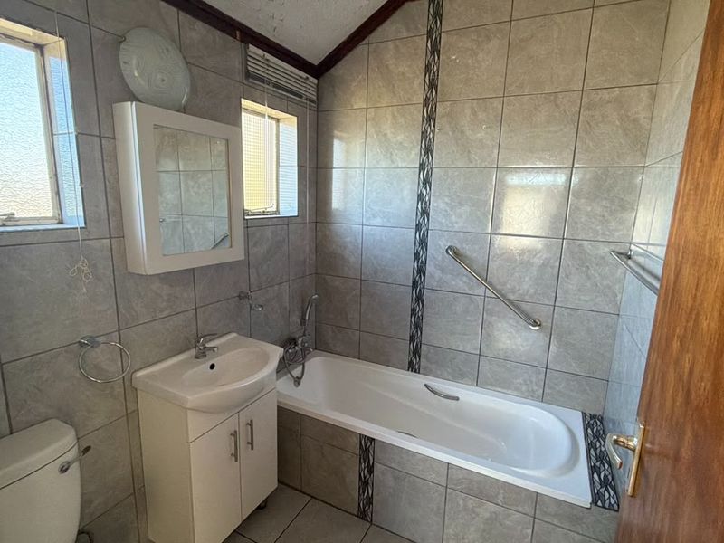 A functional bathroom featuring tiled walls and flooring, a built-in vanity with basin, a bathtub, and a wall-mounted grab rail.