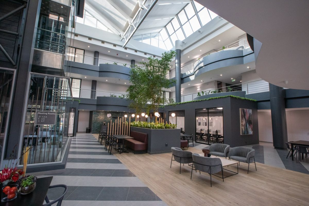 Modern commercial atrium featuring a soaring skylight, multi-level mezzanine walkways, glass elevator, and a central indoor garden area with integrated seating.