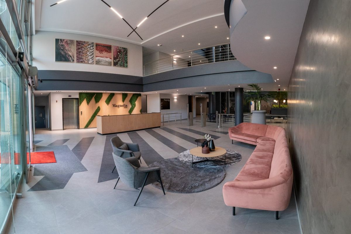 Modern commercial building entrance lobby featuring a reception desk, double-volume ceiling, mezzanine level, and contemporary architectural finishes.