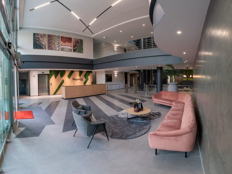 Modern commercial building entrance lobby featuring a reception desk, double-volume ceiling, mezzanine level, and contemporary architectural finishes.
