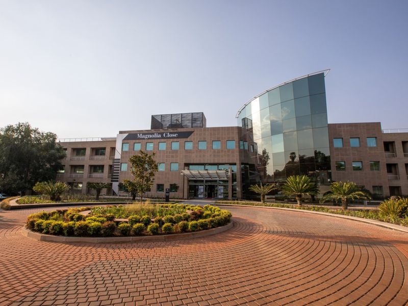 A professional exterior view of the Magnolia Close commercial office building, featuring a paved circular driveway, landscaped gardens, and a modern glass facade.