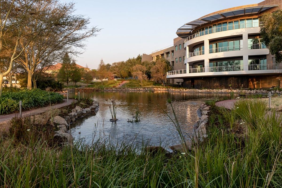 A scenic view of a modern commercial building featuring multi-level balconies overlooking a landscaped garden with a central pond and paved walkways.