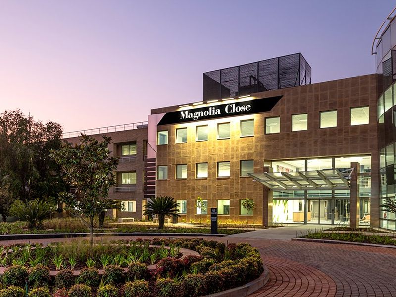 Professional exterior view of Magnolia Close commercial building featuring modern stone cladding, glass facade elements, and a well-maintained landscaped entrance area at dusk.