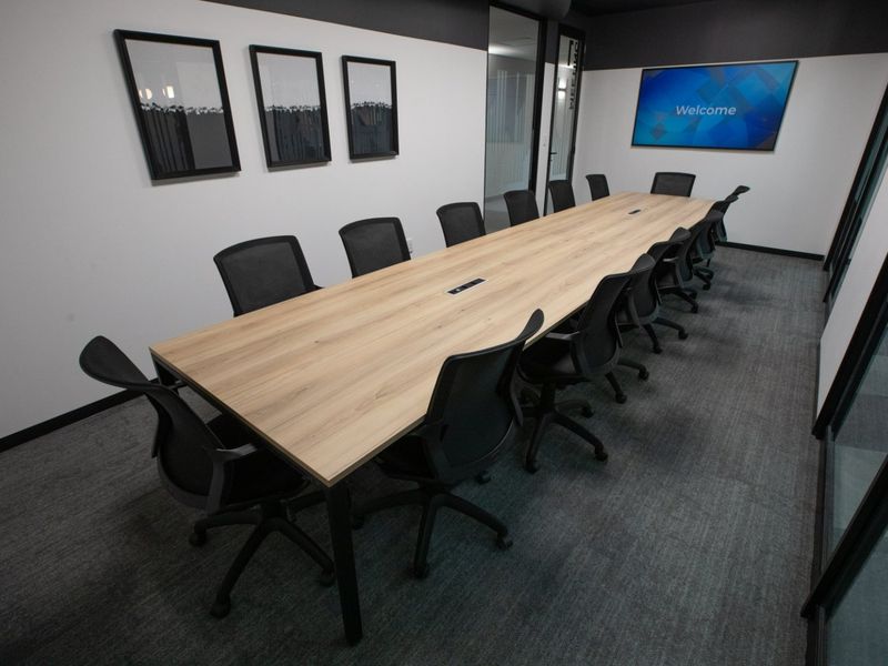 Modern commercial boardroom featuring glass partitions, integrated display screen, and professional carpeted flooring, suitable for corporate meetings and collaborative work.