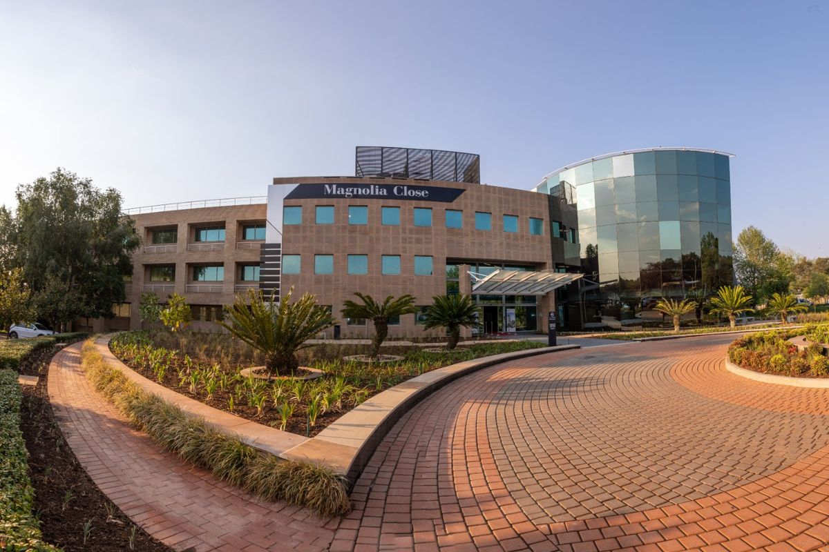 Front elevation of Magnolia Close commercial building featuring a modern glass facade, stone cladding, and a well-maintained paved driveway and landscaped entrance.