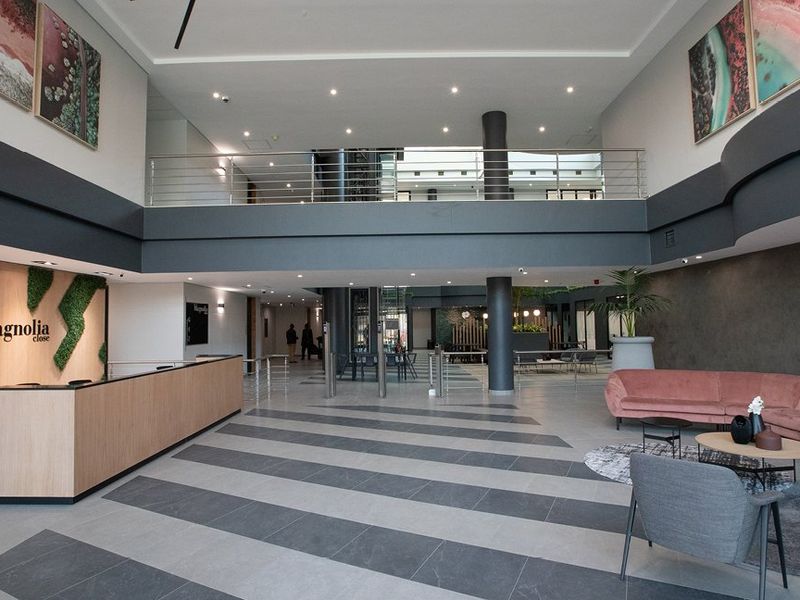 Spacious commercial lobby featuring a modern reception desk, double-volume ceiling, mezzanine level with stainless steel railings, and contemporary tiled flooring.