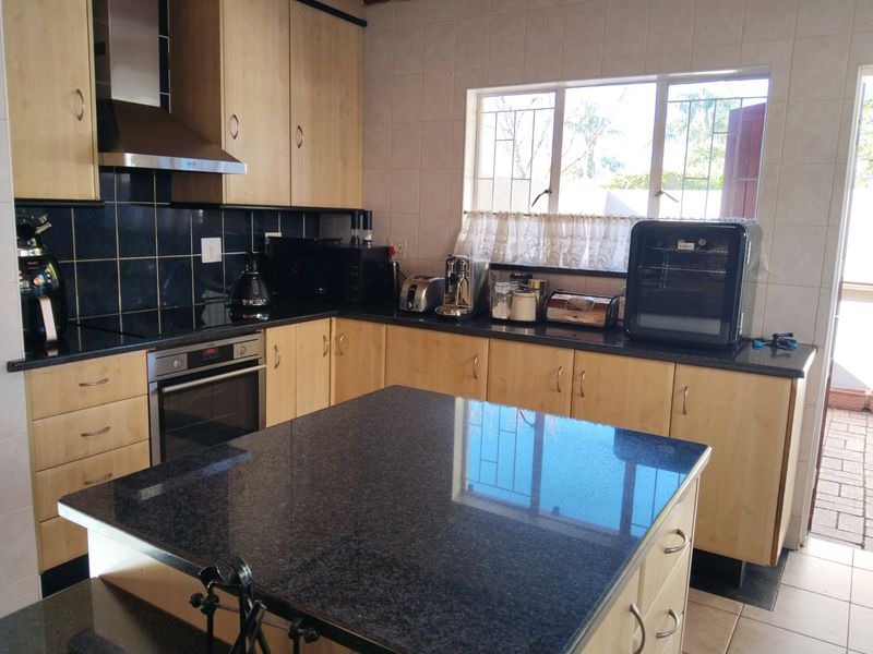 A functional kitchen featuring light wood cabinetry, dark granite countertops, a central island, and a tiled backsplash with an integrated oven and extractor fan.