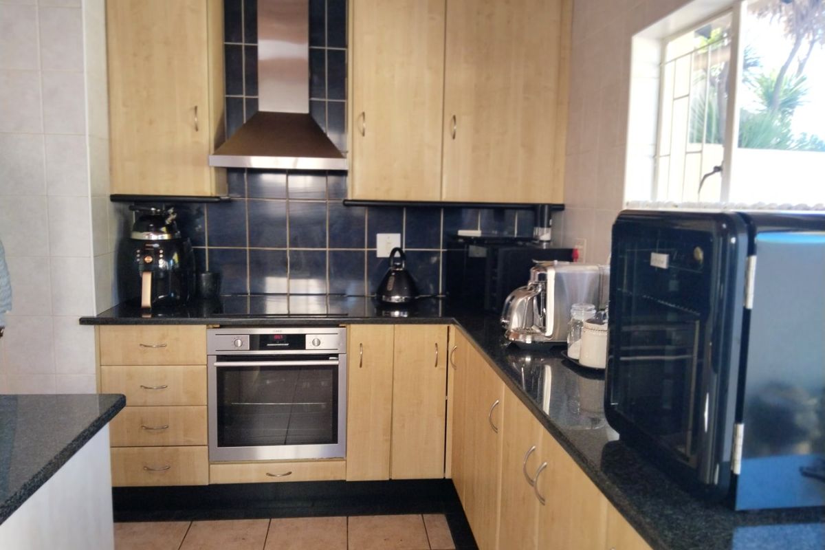 A functional kitchen featuring light wood cabinetry, dark granite countertops, a stainless steel oven, and a modern extractor fan with tiled backsplash.