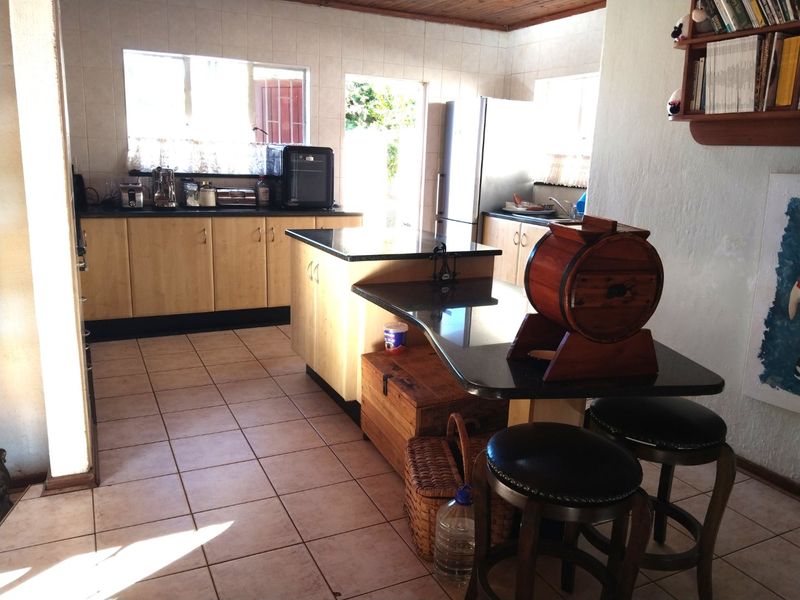 A functional kitchen featuring granite countertops, a central island, tiled flooring, and timber ceiling details, offering a practical layout with ample storage space.