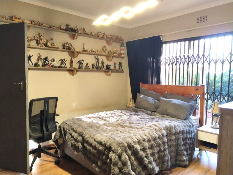 A bedroom featuring laminate flooring, a security gate on the window, and wall-mounted shelving units.