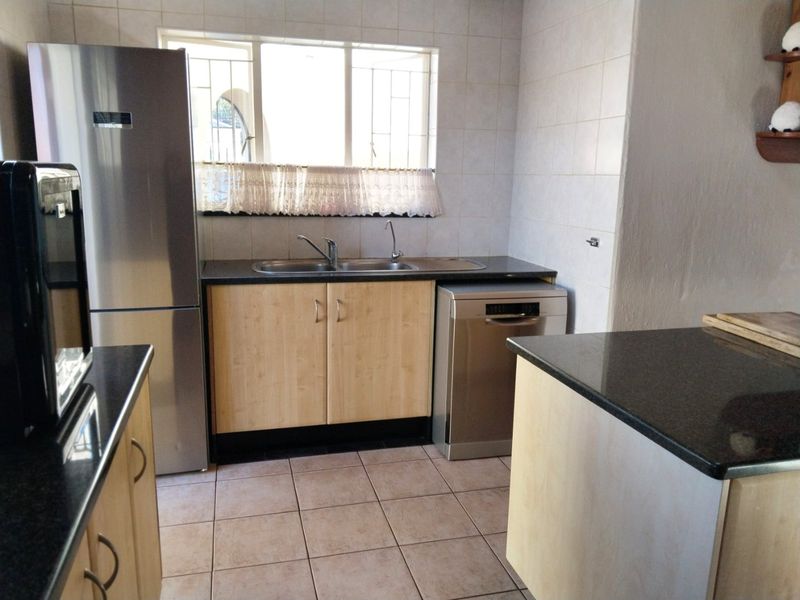 Functional kitchen featuring light wood-finish cabinetry, dark granite countertops, tiled splashbacks, and ceramic floor tiles with a double bowl sink.