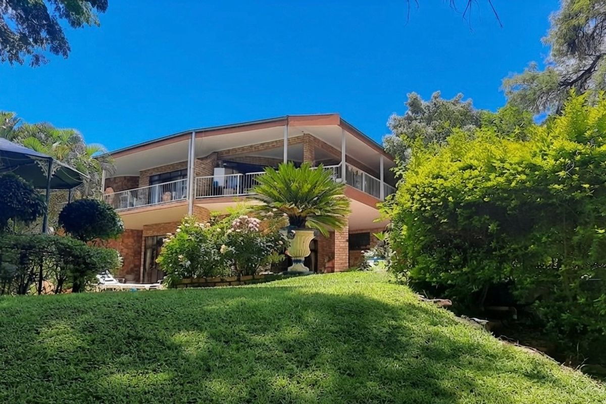 A view of the rear elevation of the house featuring a spacious covered balcony, brick construction, and a well-maintained garden.