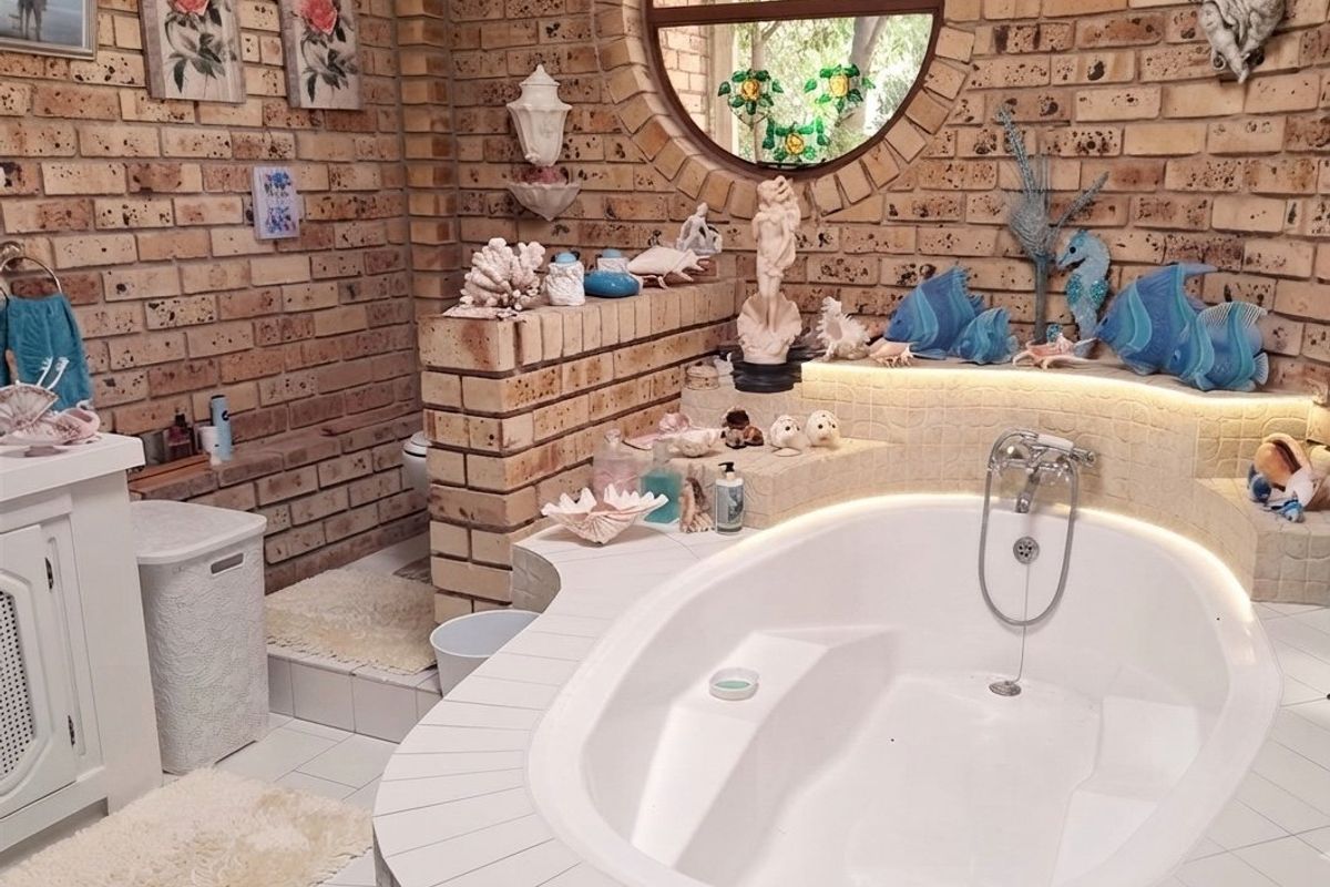 A unique bathroom featuring exposed brick walls, a circular window, and a built-in oval bathtub with integrated accent lighting.