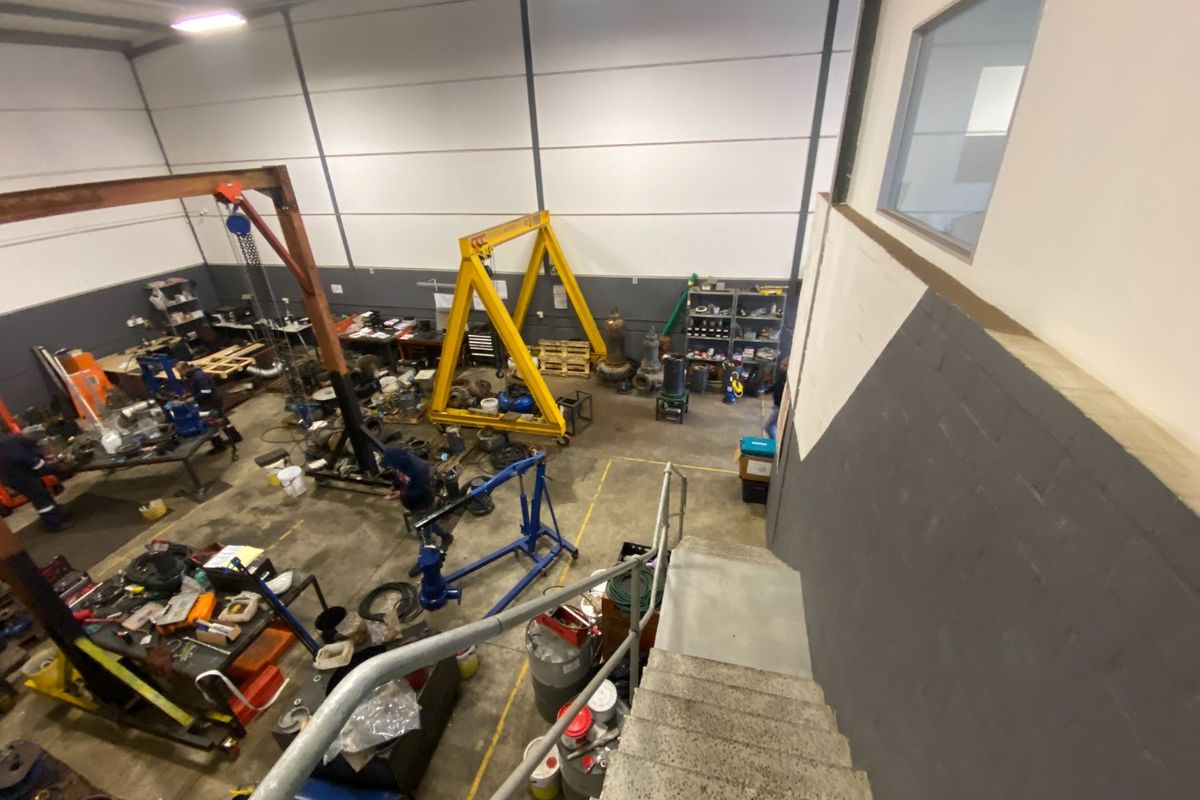 High-ceiling industrial workshop space featuring a gantry crane, concrete staircase with metal handrails, and open floor plan suitable for heavy-duty operations.