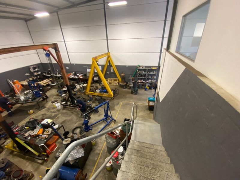 High-ceiling industrial workshop space featuring a gantry crane, concrete staircase with metal handrails, and open floor plan suitable for heavy-duty operations.