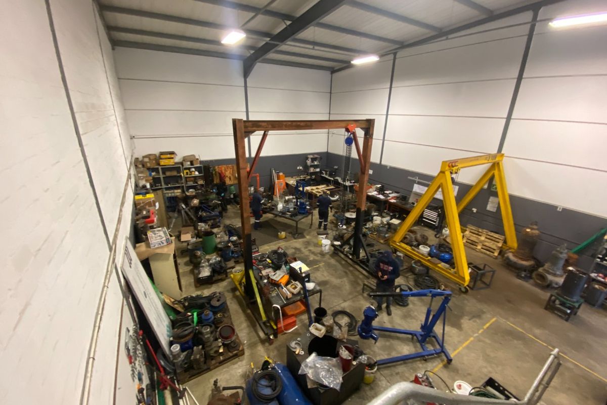 Spacious industrial workshop featuring high ceilings, exposed steel trusses, concrete flooring, and heavy-duty gantry cranes suitable for manufacturing or maintenance operations.