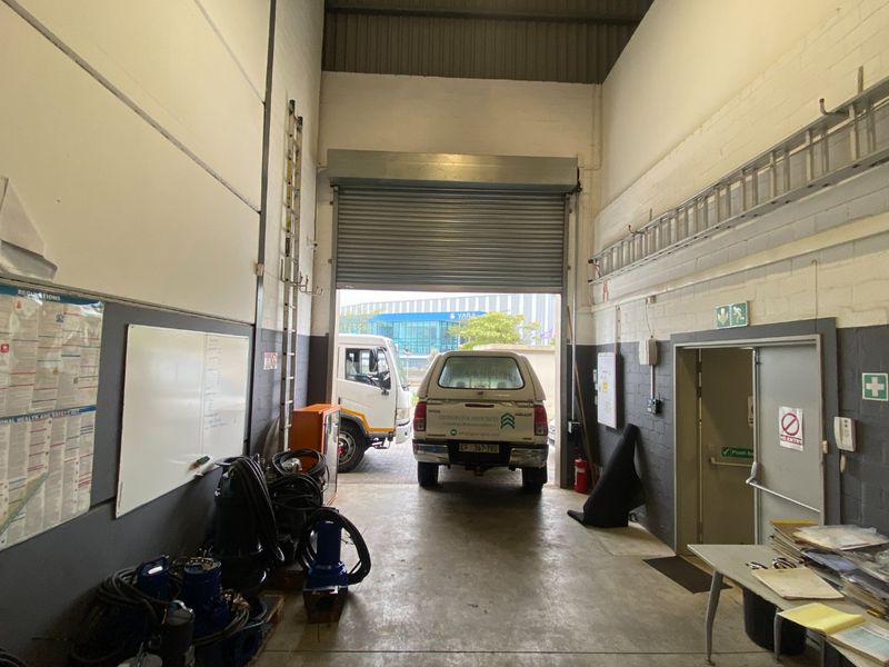 Industrial garage space featuring high ceilings, exposed steel trusses, concrete flooring, and a large roller shutter door for vehicle access.