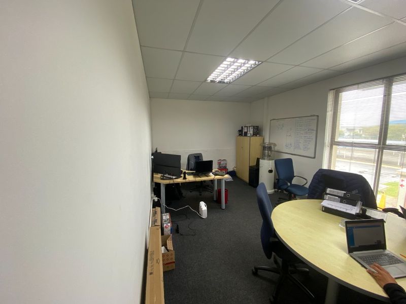 A functional office space featuring carpeted flooring, a suspended ceiling with recessed lighting, and a large window providing natural light.
