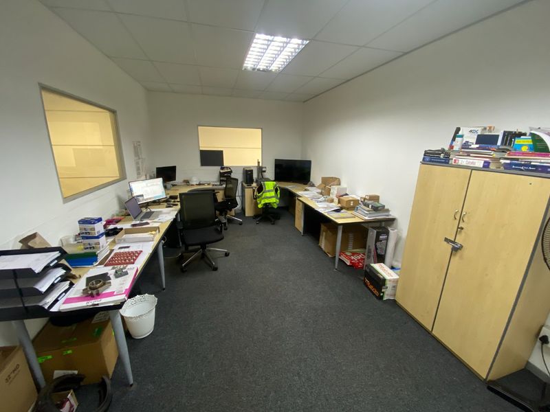 A functional industrial office space featuring suspended ceilings, recessed lighting, fitted carpeting, and internal glass partitions for visibility.