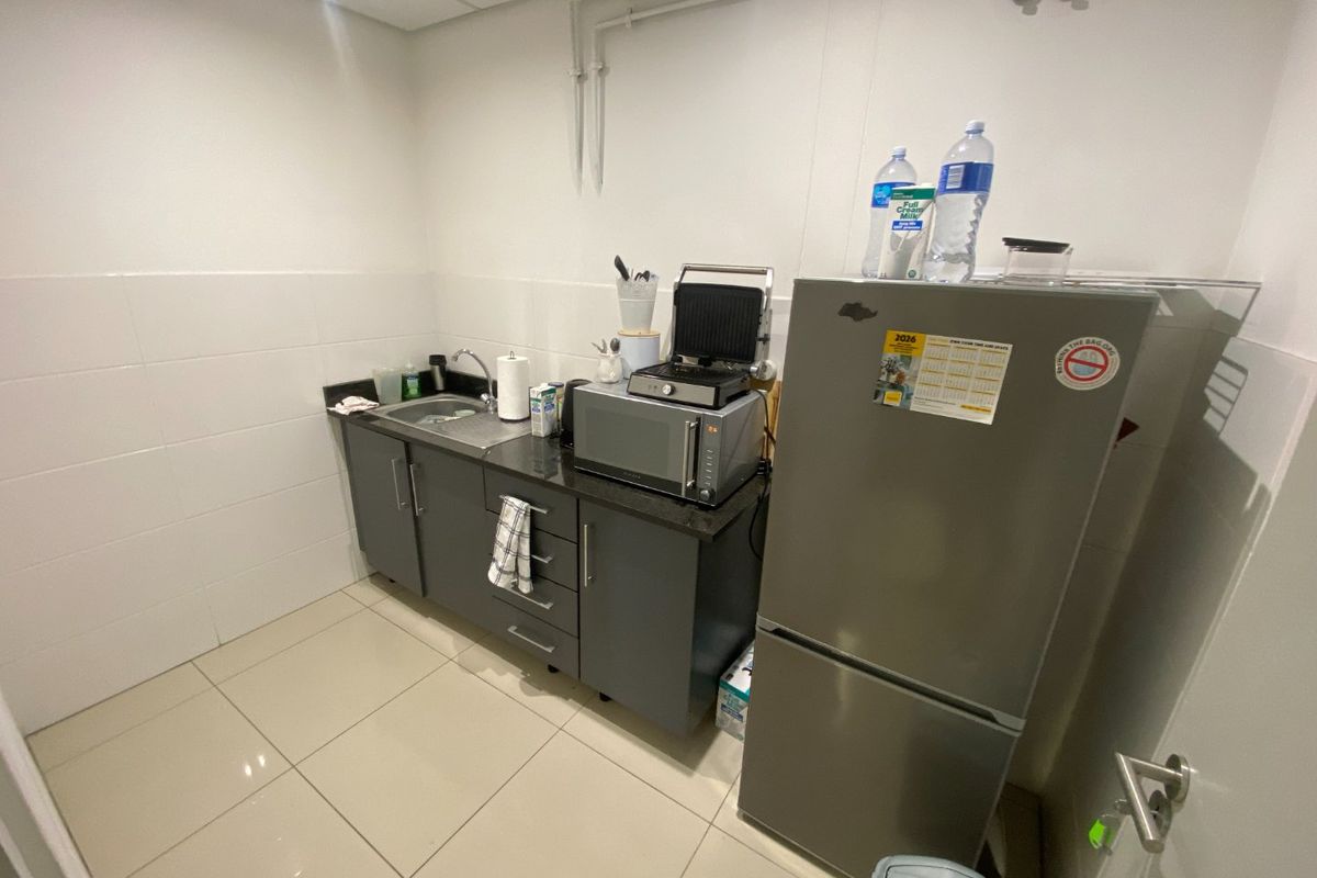 A compact industrial kitchenette featuring dark grey cabinetry, a stainless steel sink, tiled splashback, and light-colored floor tiles.