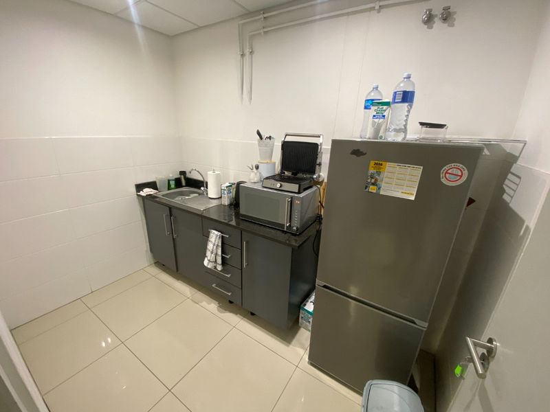 A compact industrial kitchenette featuring dark grey cabinetry, a stainless steel sink, tiled splashback, and light-colored floor tiles.
