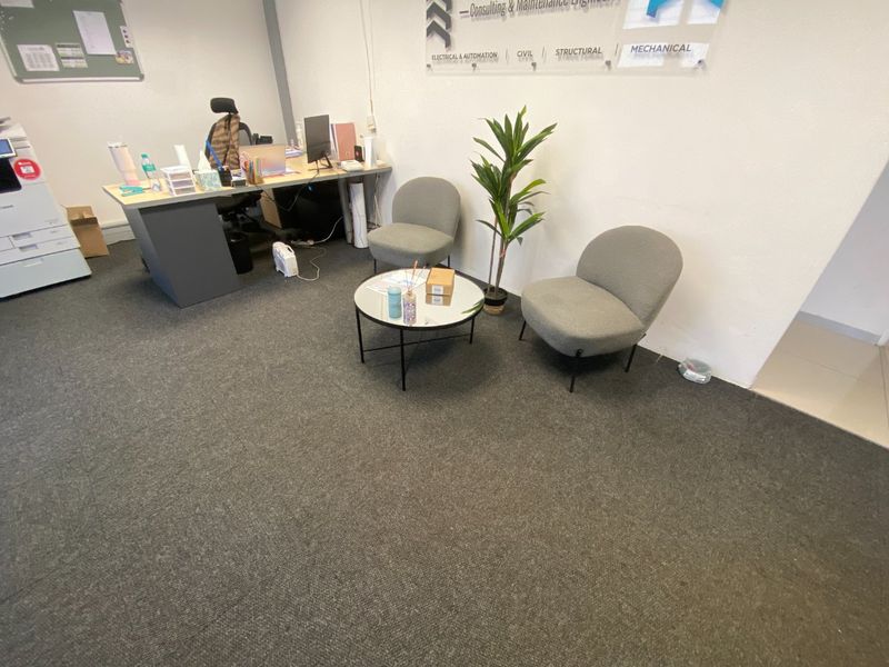 A functional office space featuring carpeted flooring and wall-mounted corporate signage, suitable for professional administrative or consulting use.
