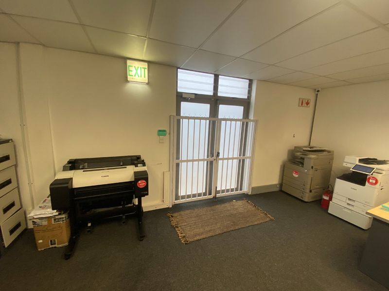Functional office space featuring a suspended ceiling, carpeted flooring, and a secure access door with a fitted security gate.