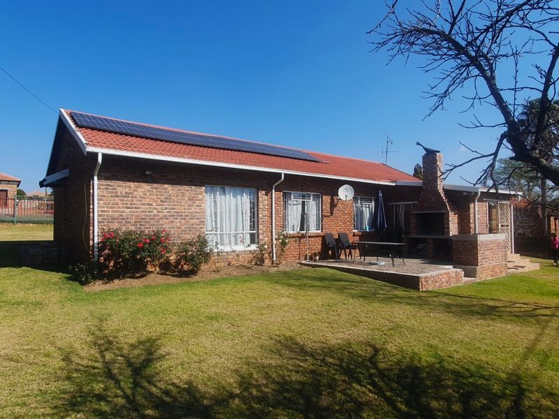 Rear view of a face brick house featuring a paved patio with a built-in braai, solar panels on the roof, and a well-maintained garden.