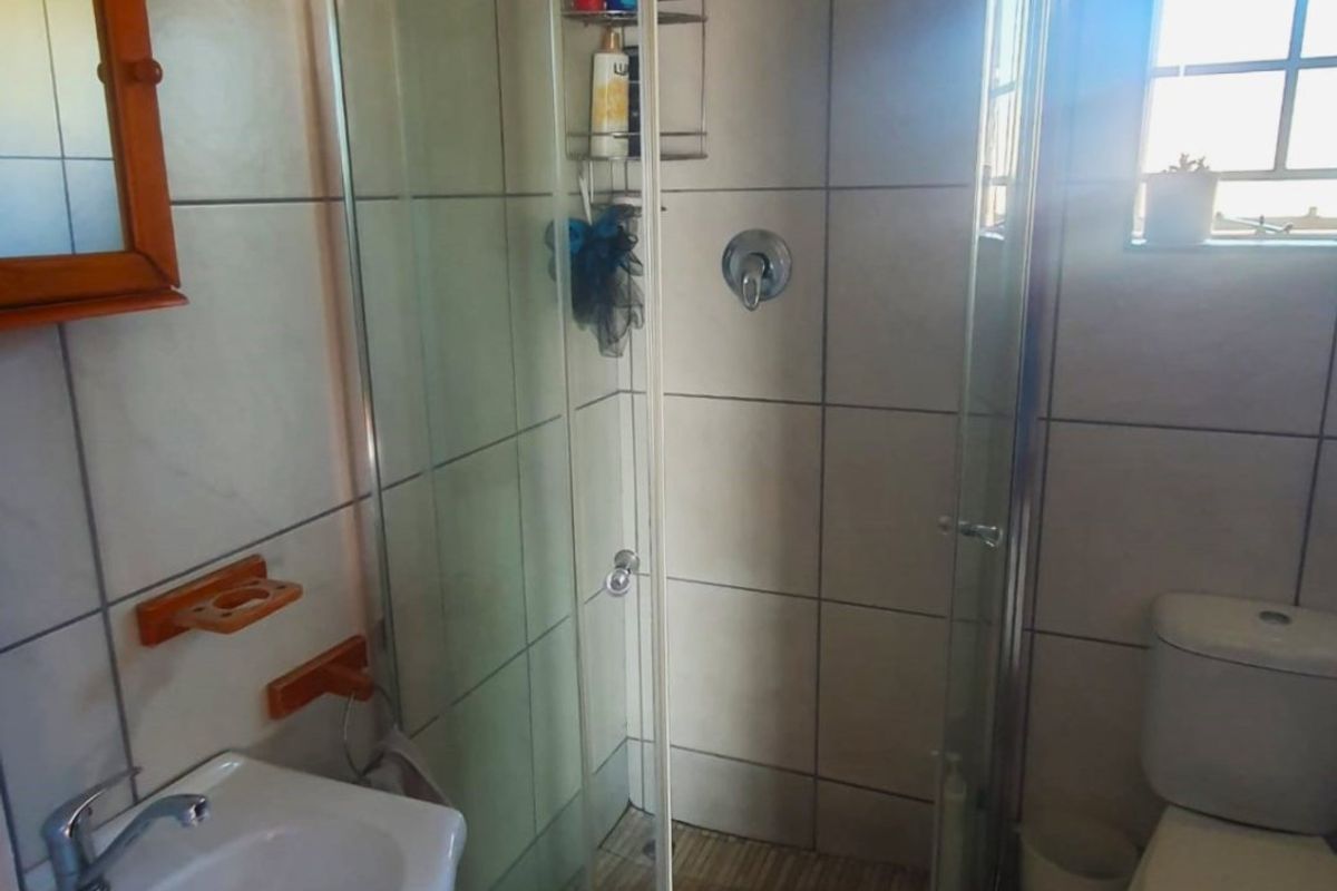 A functional bathroom featuring a curved glass shower enclosure, wall-mounted basin, and toilet with neutral wall and floor tiling.