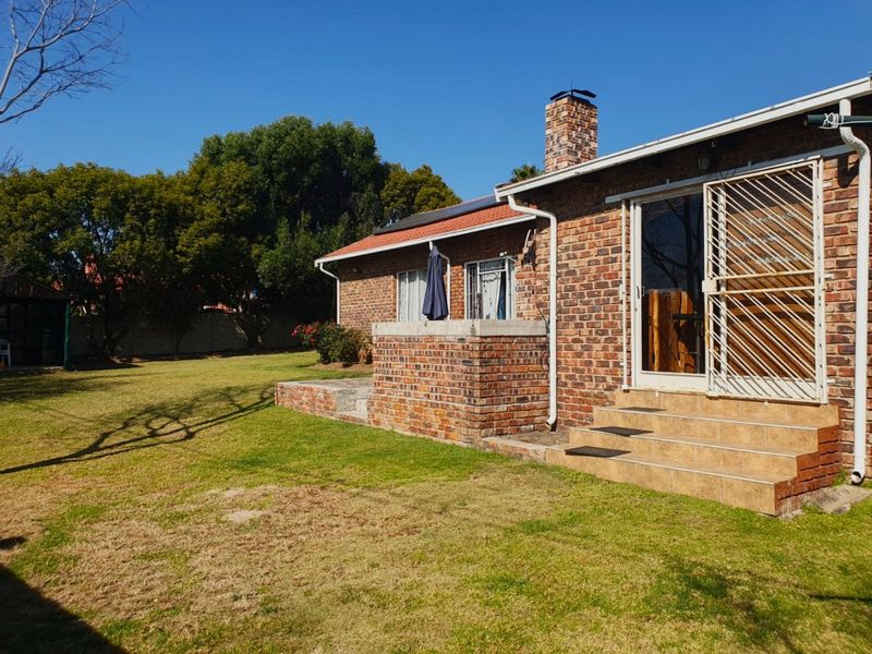 Rear view of a brick house featuring a chimney, tiled patio steps, security gate, and a spacious lawn area.
