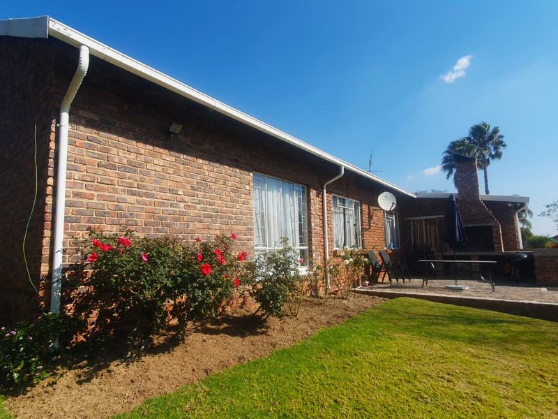 Rear view of the house featuring a face brick facade, a paved patio area with a built-in braai, and a well-maintained garden.