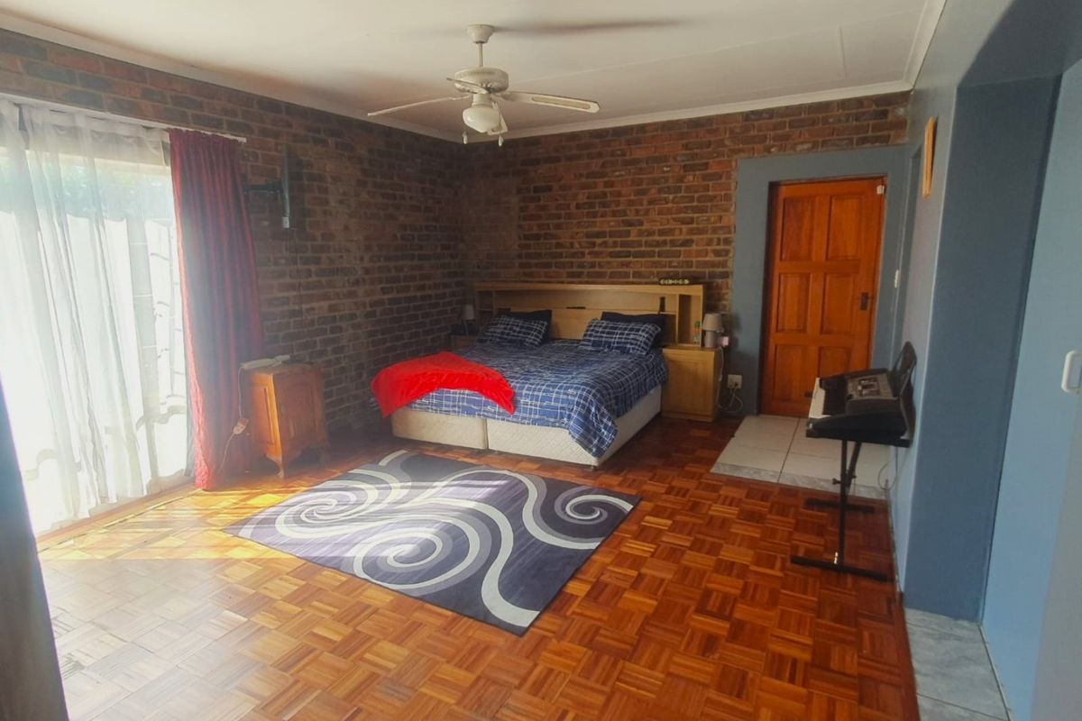 Spacious bedroom featuring exposed brick walls, warm parquet flooring, and a ceiling fan, with direct access to the outdoors via a sliding glass door.