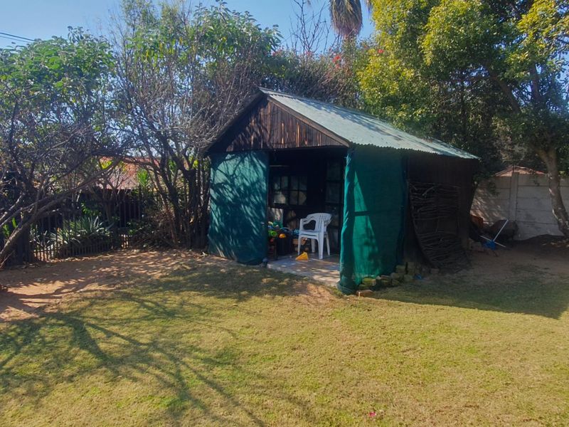 A backyard garden featuring a weathered timber shed with a corrugated metal roof, surrounded by mature trees and lawn.